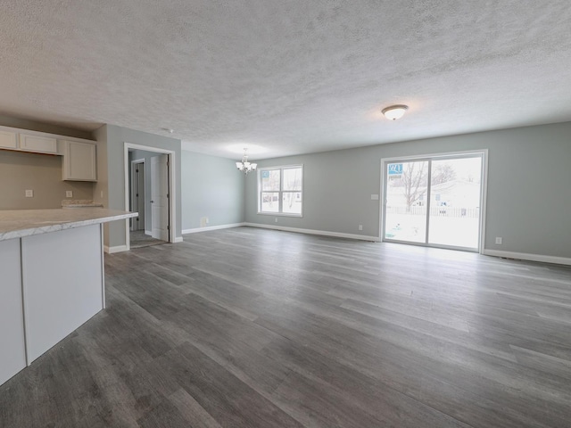 unfurnished living room with baseboards, dark wood-type flooring, a textured ceiling, and an inviting chandelier