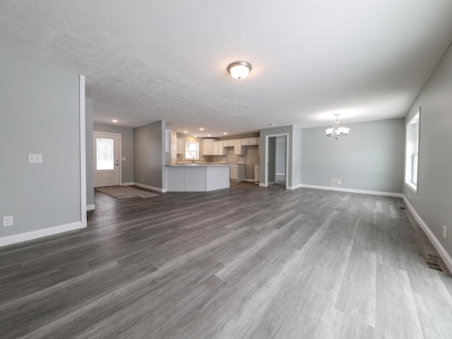 unfurnished living room featuring dark wood finished floors, visible vents, an inviting chandelier, a textured ceiling, and baseboards