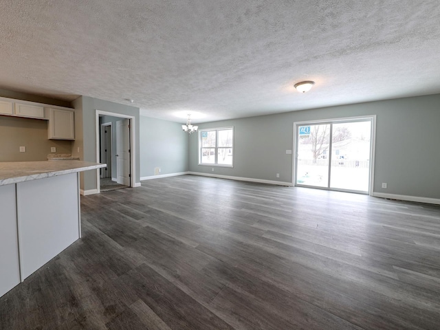 unfurnished living room with dark wood-style floors, a textured ceiling, baseboards, and an inviting chandelier