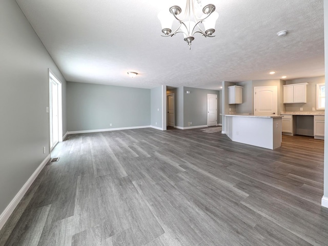 unfurnished living room featuring dark wood-style floors, baseboards, visible vents, and a notable chandelier