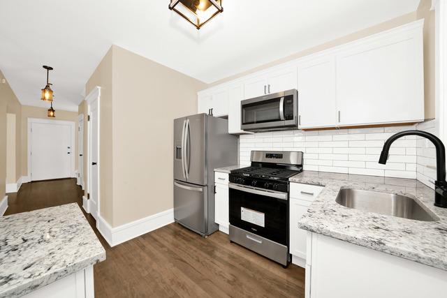 kitchen featuring light stone counters, pendant lighting, appliances with stainless steel finishes, white cabinets, and a sink