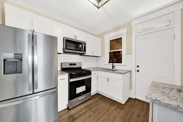 kitchen with light stone counters, a sink, white cabinets, appliances with stainless steel finishes, and dark wood finished floors