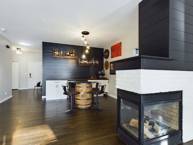 bar with baseboards, dark wood-style floors, bar, hanging light fixtures, and a brick fireplace