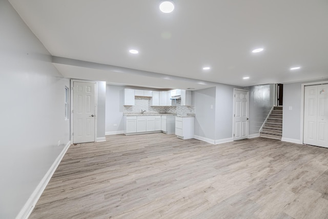 unfurnished living room with light wood-style floors, baseboards, and stairs