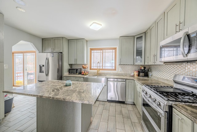 kitchen with light stone counters, stainless steel appliances, decorative backsplash, light wood finished floors, and glass insert cabinets