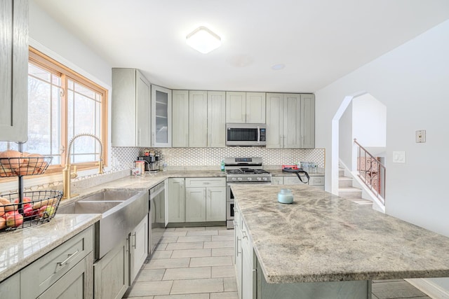 kitchen with stainless steel appliances, tasteful backsplash, glass insert cabinets, a sink, and light stone countertops