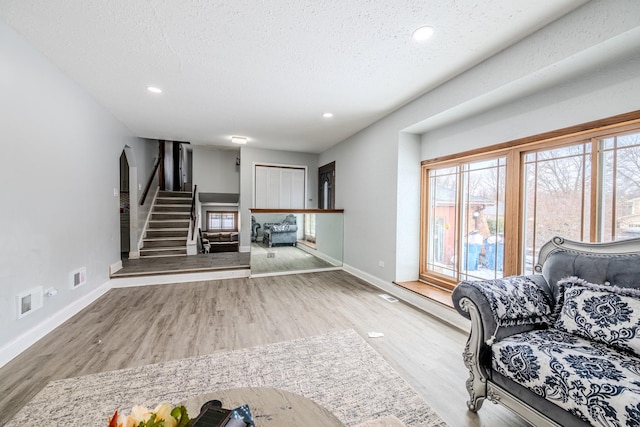 unfurnished living room with visible vents, light wood-style floors, a textured ceiling, baseboards, and stairs