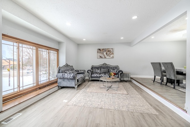 living room with a textured ceiling, light wood-style flooring, visible vents, and baseboards