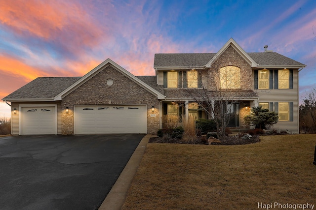 view of front of house with a garage, driveway, a shingled roof, and a lawn