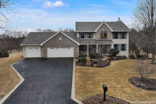 traditional home featuring a garage, driveway, roof with shingles, and a front yard