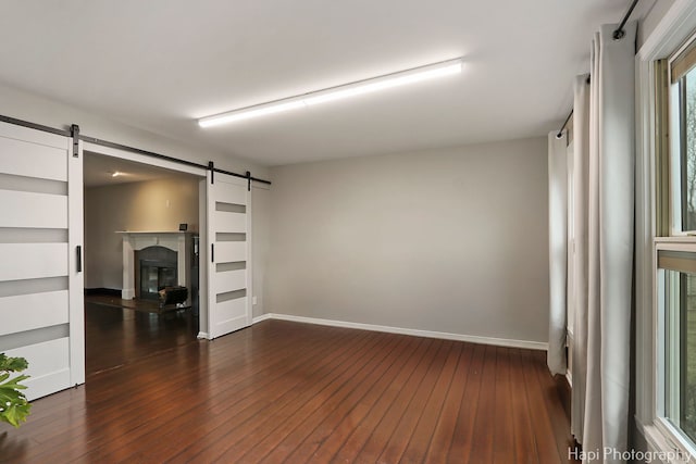 unfurnished room featuring a barn door, dark wood-type flooring, and baseboards