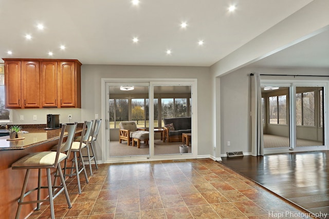 kitchen featuring plenty of natural light, visible vents, a kitchen breakfast bar, and dark stone counters