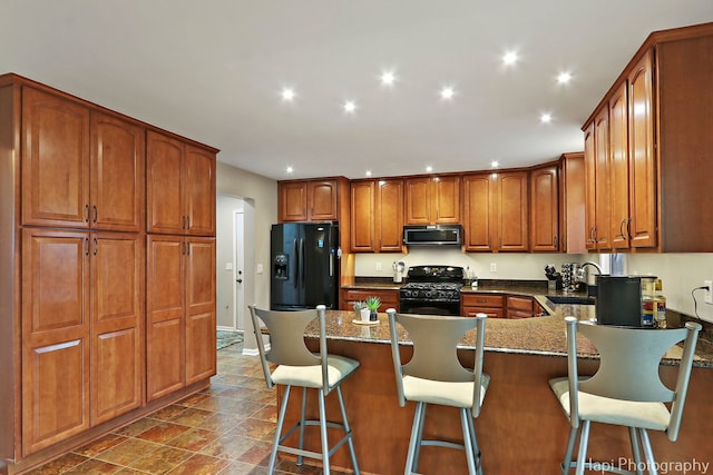 kitchen with a peninsula, a sink, brown cabinets, black appliances, and a kitchen bar