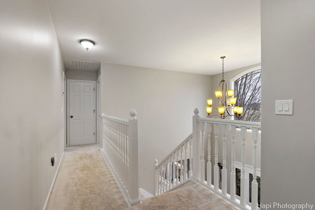 hall with baseboards, visible vents, an upstairs landing, carpet floors, and a notable chandelier