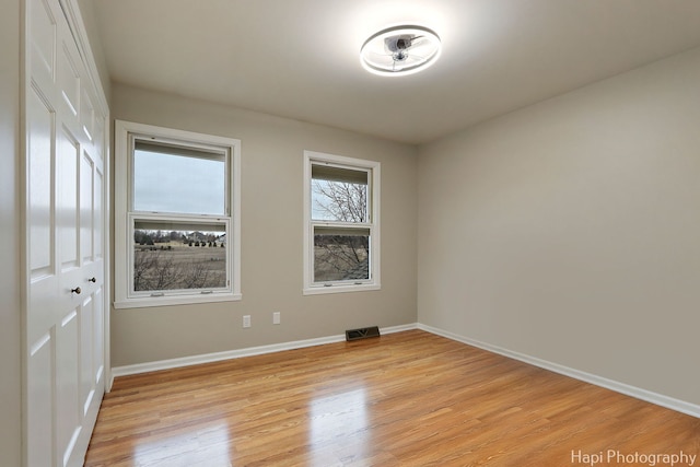 unfurnished room featuring light wood-type flooring, visible vents, and baseboards