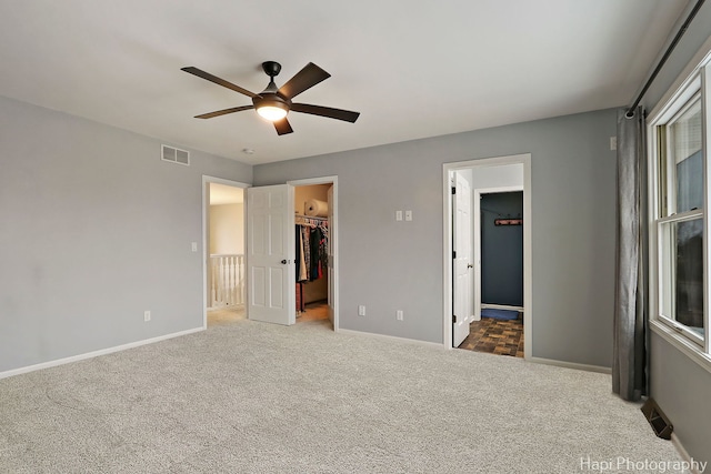 unfurnished bedroom with carpet, a walk in closet, visible vents, ceiling fan, and baseboards