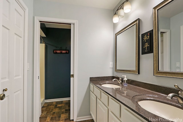 bathroom with double vanity, baseboards, walk in shower, and a sink