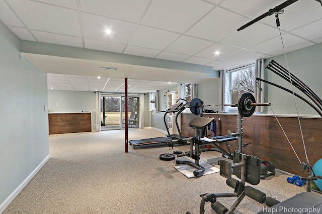 exercise area featuring a drop ceiling, plenty of natural light, carpet flooring, and wooden walls