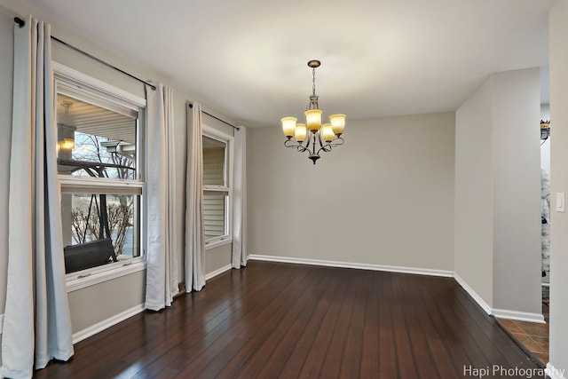 unfurnished room featuring baseboards, dark wood finished floors, and a notable chandelier