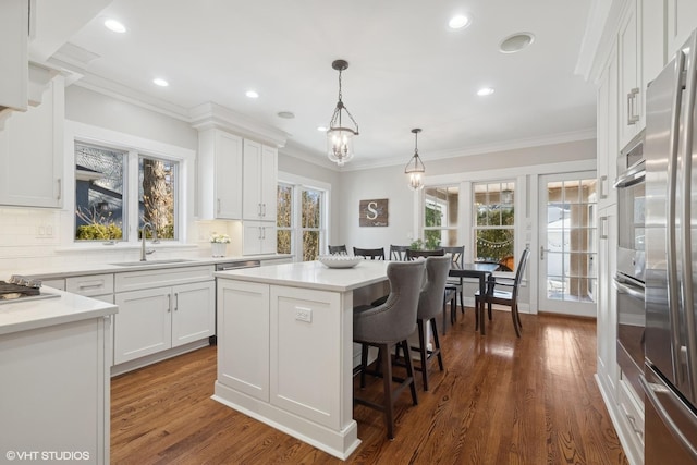 kitchen with a sink, white cabinetry, a healthy amount of sunlight, appliances with stainless steel finishes, and crown molding