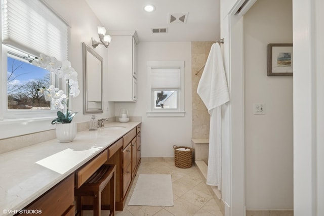 bathroom with tiled shower, vanity, and visible vents