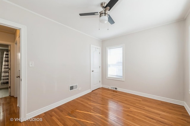 empty room with baseboards, wood-type flooring, visible vents, and crown molding