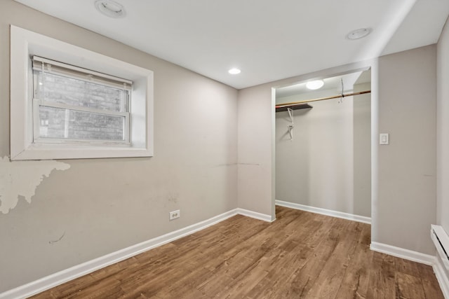 unfurnished bedroom with a baseboard radiator, a closet, recessed lighting, wood finished floors, and baseboards