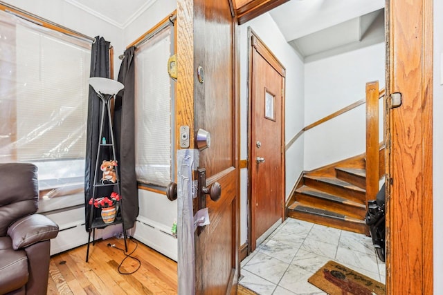 foyer featuring a baseboard heating unit, marble finish floor, crown molding, and stairs