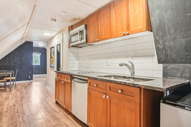 kitchen with light wood-style flooring, stainless steel appliances, a sink, backsplash, and brown cabinetry