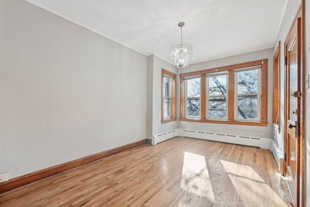 empty room with a chandelier, ornamental molding, light wood-style flooring, and baseboards