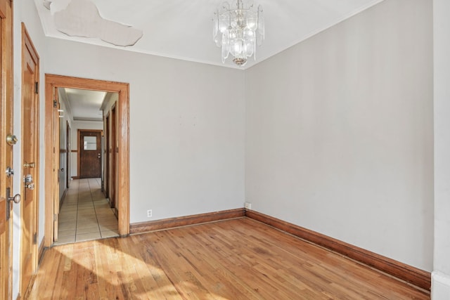 spare room with a notable chandelier, crown molding, baseboards, and wood finished floors