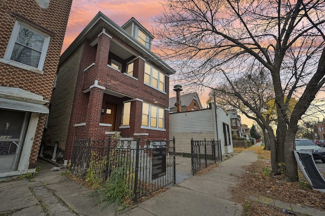 property exterior at dusk featuring brick siding and a fenced front yard