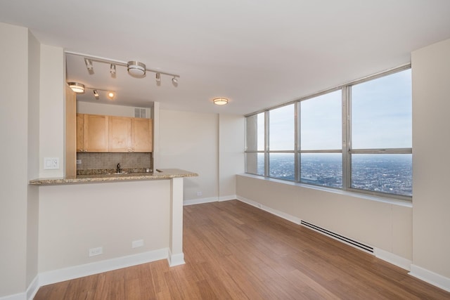 interior space with a baseboard radiator, light brown cabinets, wood finished floors, baseboards, and backsplash