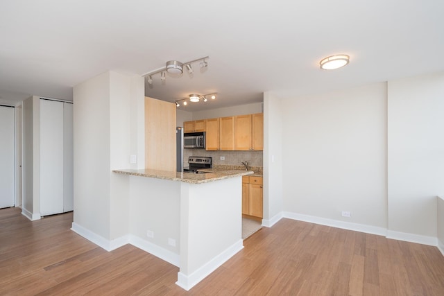 kitchen with stainless steel appliances, tasteful backsplash, light brown cabinets, light wood-type flooring, and baseboards