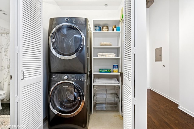 clothes washing area featuring stacked washer and dryer, baseboards, laundry area, and wood finished floors