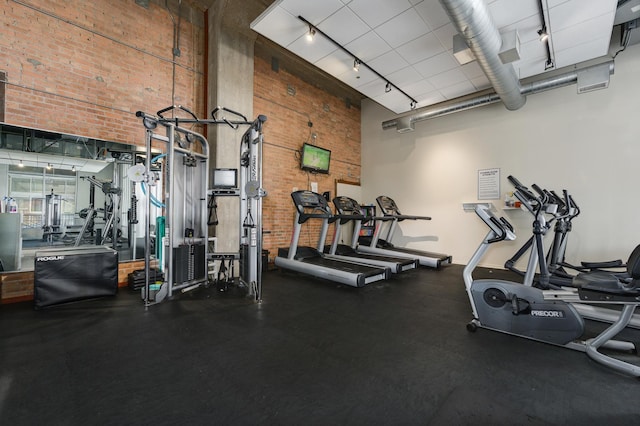 gym featuring a towering ceiling, brick wall, and track lighting