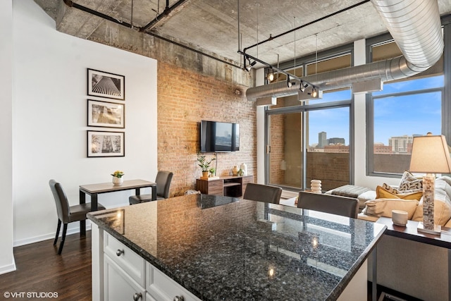 kitchen with a center island, dark wood-type flooring, white cabinets, brick wall, and dark stone counters