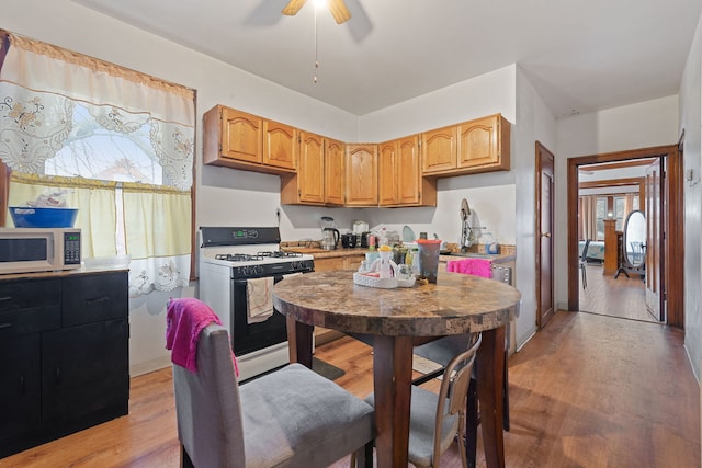 kitchen featuring white microwave, gas stove, a sink, and light wood-style floors