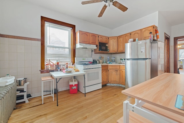 kitchen with white range with gas cooktop, light wood-style flooring, freestanding refrigerator, under cabinet range hood, and black microwave