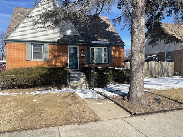 view of front of property featuring a shingled roof, fence, and brick siding