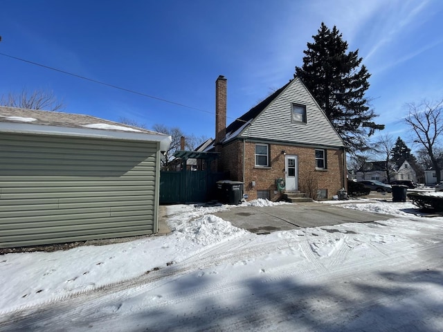 snow covered house with entry steps, a chimney, central AC unit, and brick siding