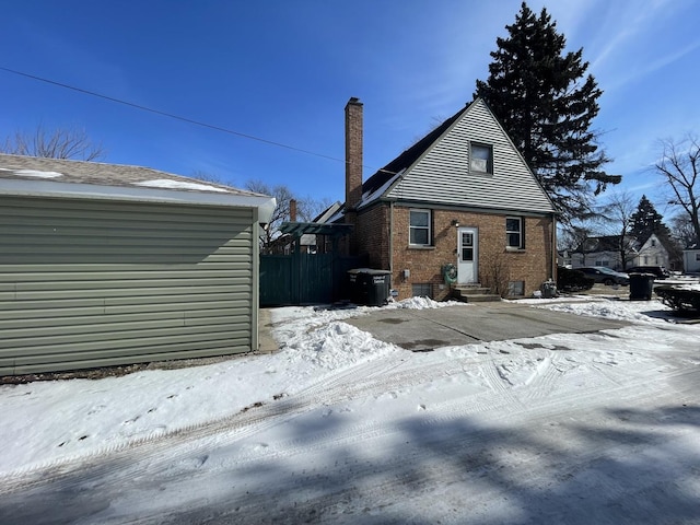 snow covered rear of property with entry steps, brick siding, and a chimney