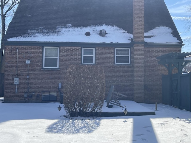 snow covered back of property featuring brick siding and a chimney