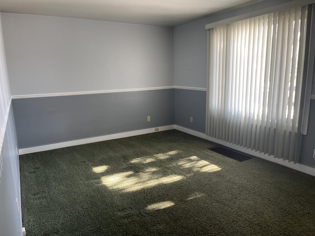 unfurnished room with baseboards, visible vents, and dark carpet