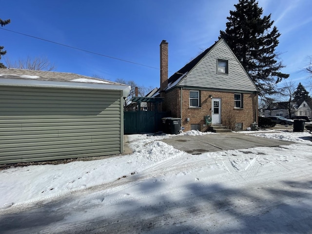 snow covered rear of property with entry steps, a chimney, fence, and brick siding