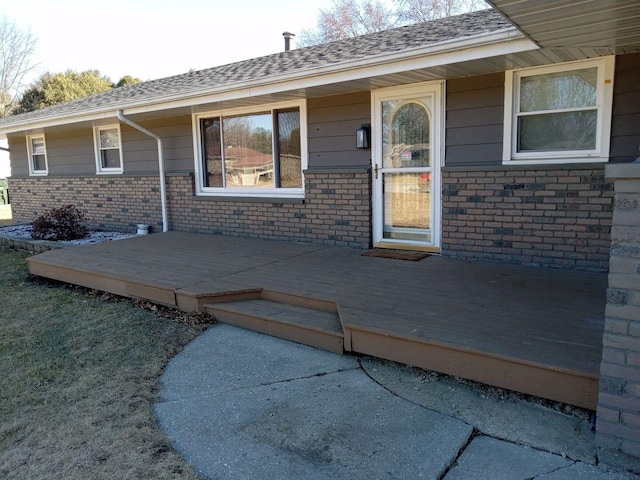 view of exterior entry featuring brick siding and roof with shingles