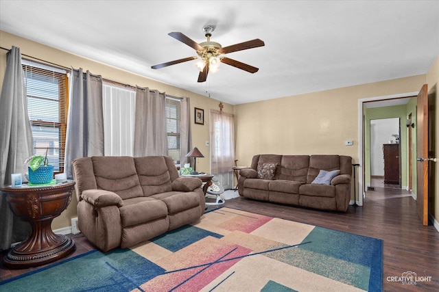 living room featuring ceiling fan, baseboards, dark wood-type flooring, and a wealth of natural light