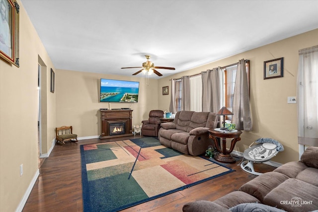 living room with dark wood-style floors, ceiling fan, baseboards, and a glass covered fireplace