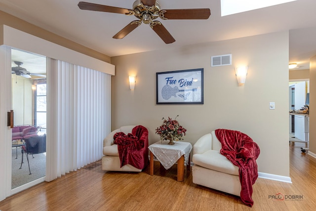 living area featuring a ceiling fan, wood finished floors, visible vents, and baseboards