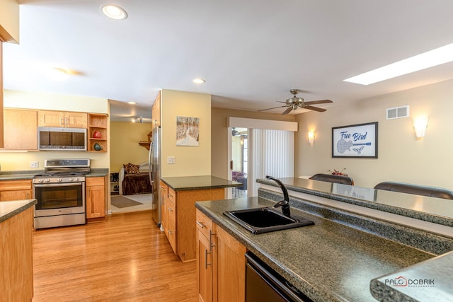 kitchen featuring stainless steel appliances, a sink, visible vents, light wood finished floors, and dark countertops